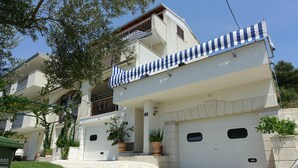 Ein zweigeschossiges Wohnhaus mit weißer Fassade, einem Balkon mit blau-weiß gestreifter Markise und einer Garage mit zwei Toren.