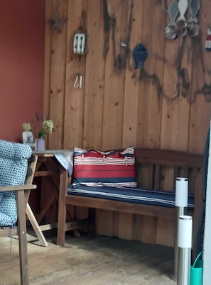 A wooden bench with striped cushions, a small table with a vase of flowers, and a metal water bottle. - Bungalow 2 - Apartment and bungalow in Trassenheide (Zinnowitz)