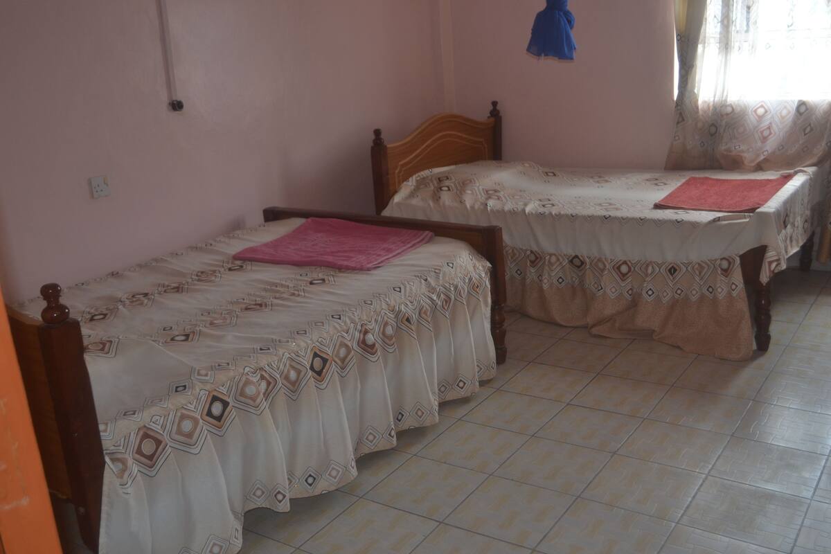 Duas camas de solteiro com roupa de cama estampada, uma toalha rosa e uma cabeceira de madeira.