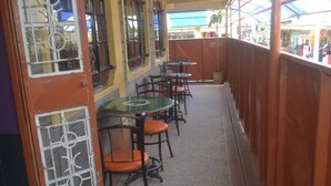 A covered outdoor seating area with tables and chairs, a tiled floor, and a view of the street. - Maendeleo Parkview Hotel (Narok)