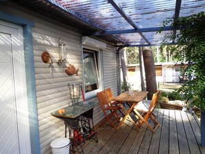 A covered patio with a wooden table and chairs, a lantern, and a fish-shaped decoration on the wall. - Bungalow 1 - Apartment and bungalow in Trassenheide (Zinnowitz)