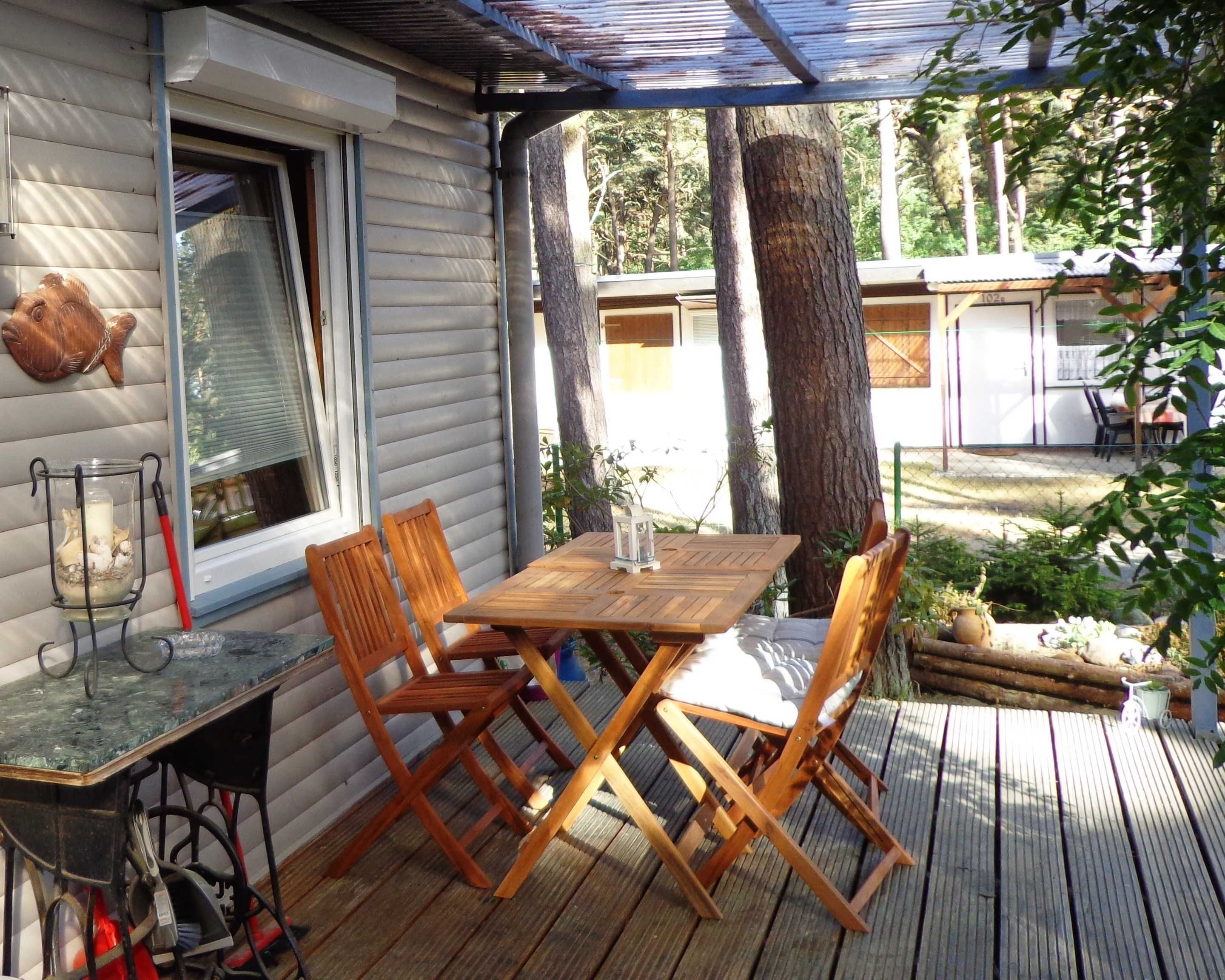 Eine Holzterrasse mit Tisch und Stühlen, einer Laterne und einer Fischdekoration an der Wand.