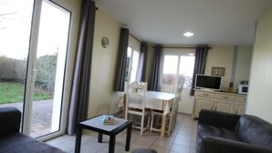 Ein Wohnzimmer mit einer Couch, einem kleinen Tisch und einem Essbereich mit Stühlen und einem Tisch. Es gibt eine Küchenzeile mit Schränken und einem Fernseher.