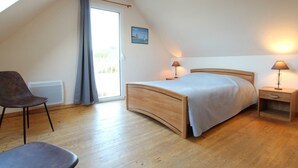 Ein Schlafzimmer mit einem hölzernen Bett, zwei Nachttischen mit Lampen, einem Sessel, einer Heizung und einem Fenster mit Vorhängen.