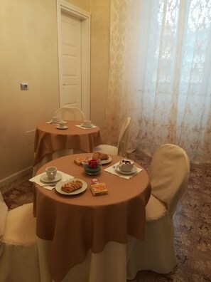 A dining area with two round tables covered with brown tablecloths, white chairs, and a variety of food and drink items. - B&B Giorgia (Tropea)
