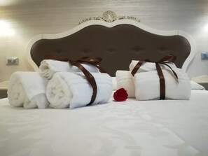 A neatly made bed with rolled white towels tied with brown ribbons and a single red rose. - B&B Giorgia (Tropea)