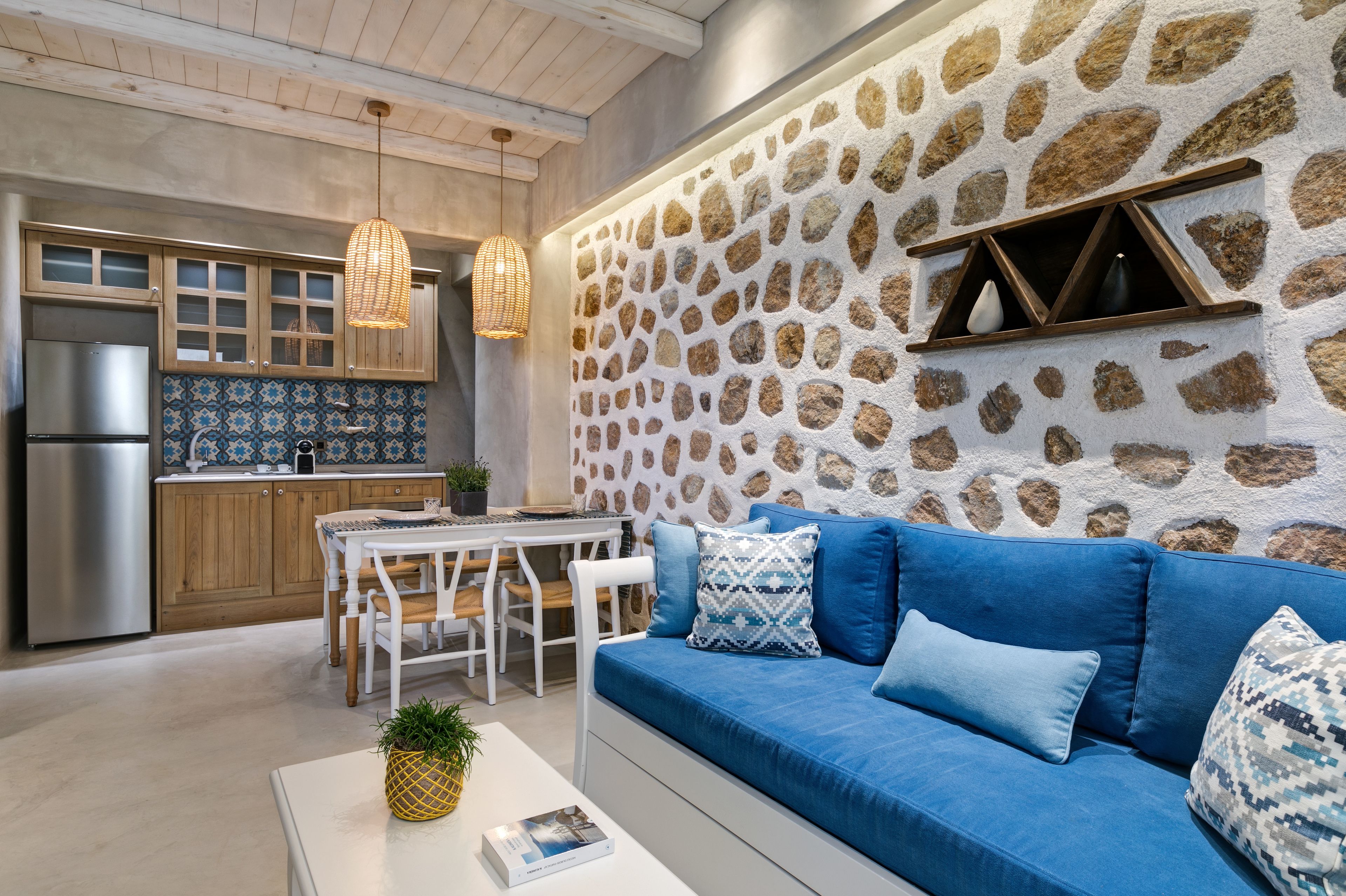 A modern kitchen with stone wall backsplash, wooden cabinets, and a blue sofa with patterned cushions.
