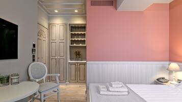 Una habitación de hotel con cama, escritorio, silla, televisor y estante con objetos decorativos.