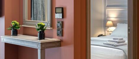 A hotel room with a large mirror, bedside table with two potted plants, a bed with a white comforter, and a nightstand with a lamp.