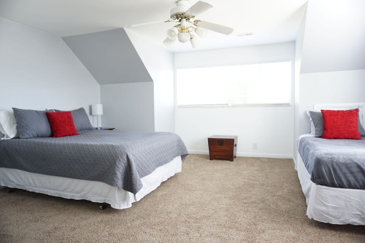 A bedroom with two beds, a ceiling fan, a window, and a small wooden chest.
