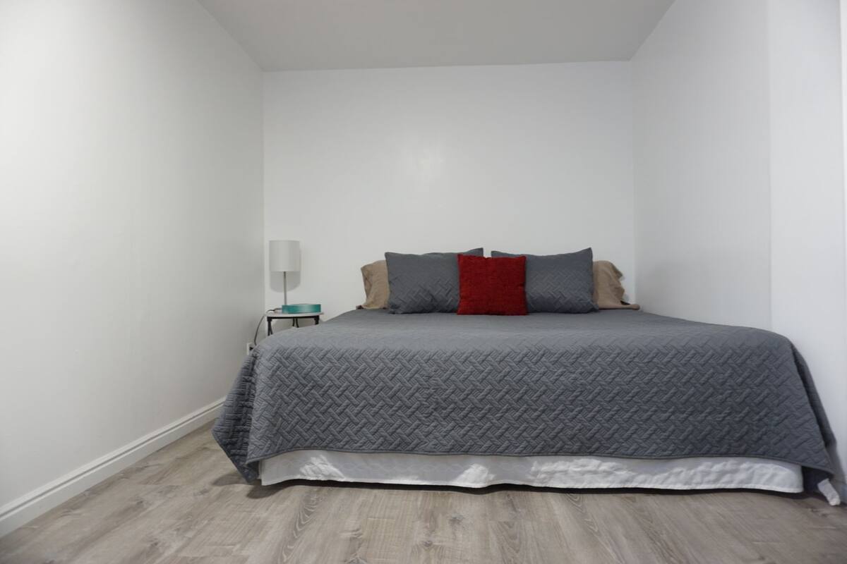 A small, neatly arranged bedroom with a bed, a bedside table, and a lamp.