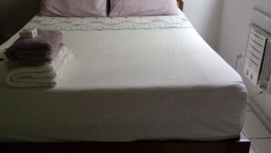 A bed with a floral bedspread, two pillows, and a stack of folded towels. - Apartamento Copacabana Vista mar (Rio de Janeiro)