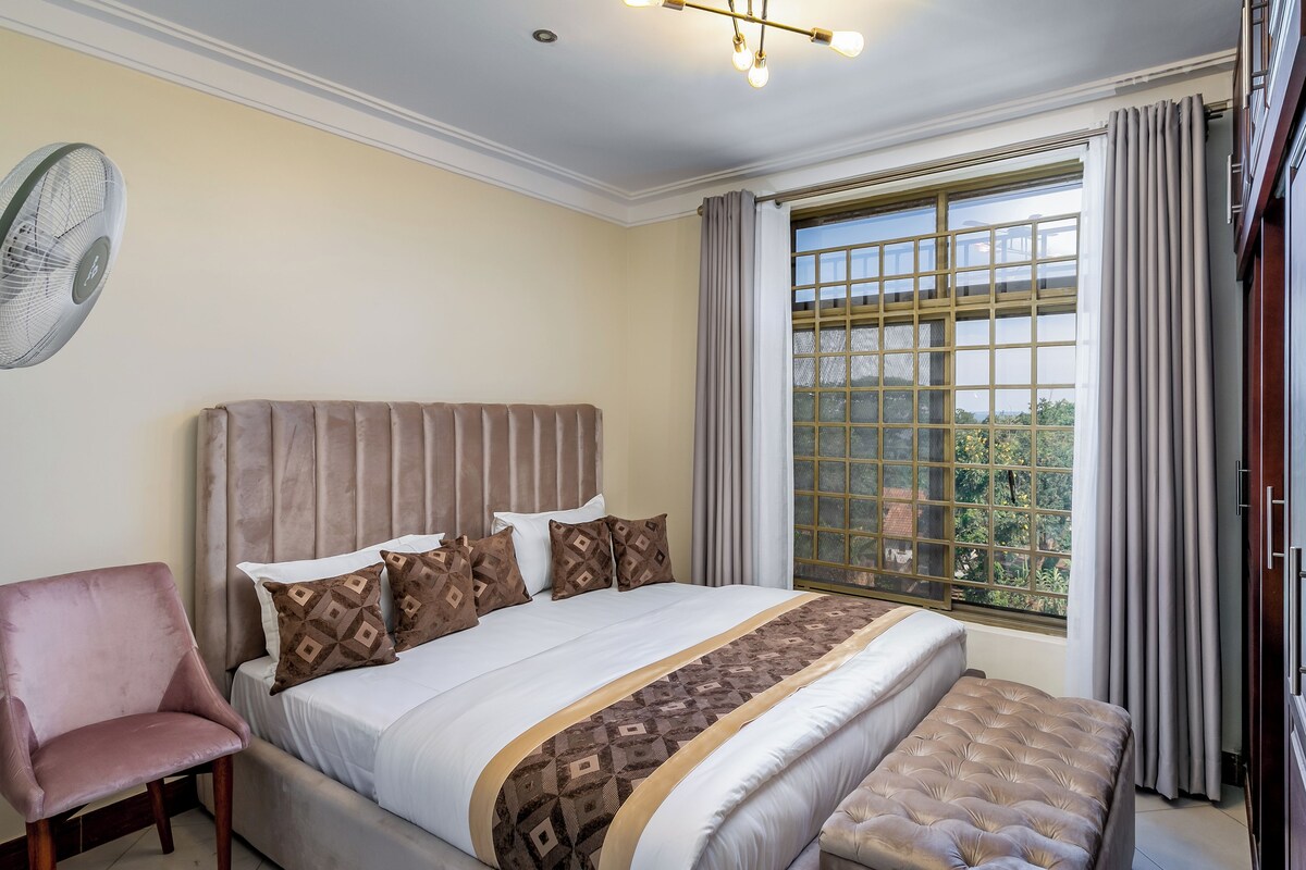 A bedroom with a large bed, a chair, a window with curtains, and a ceiling fan.