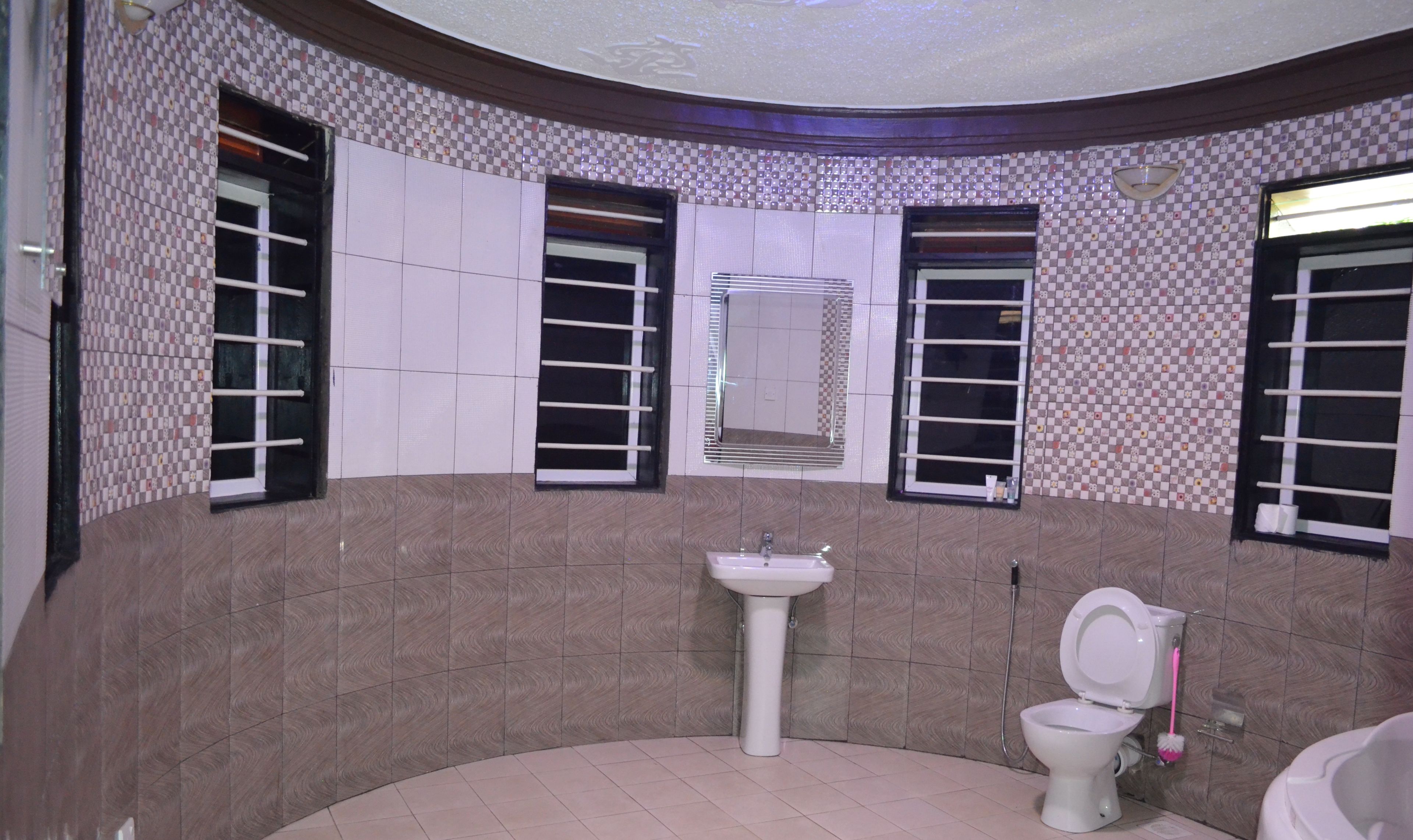 Ein Badezimmer mit Waschbecken, Toilette und Badewanne. Zwei Fenster mit Jalousien und ein Spiegel über dem Waschbecken.