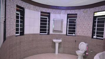 Ein Badezimmer mit Waschbecken, Toilette und Badewanne. Zwei Fenster mit Jalousien und ein Spiegel über dem Waschbecken.