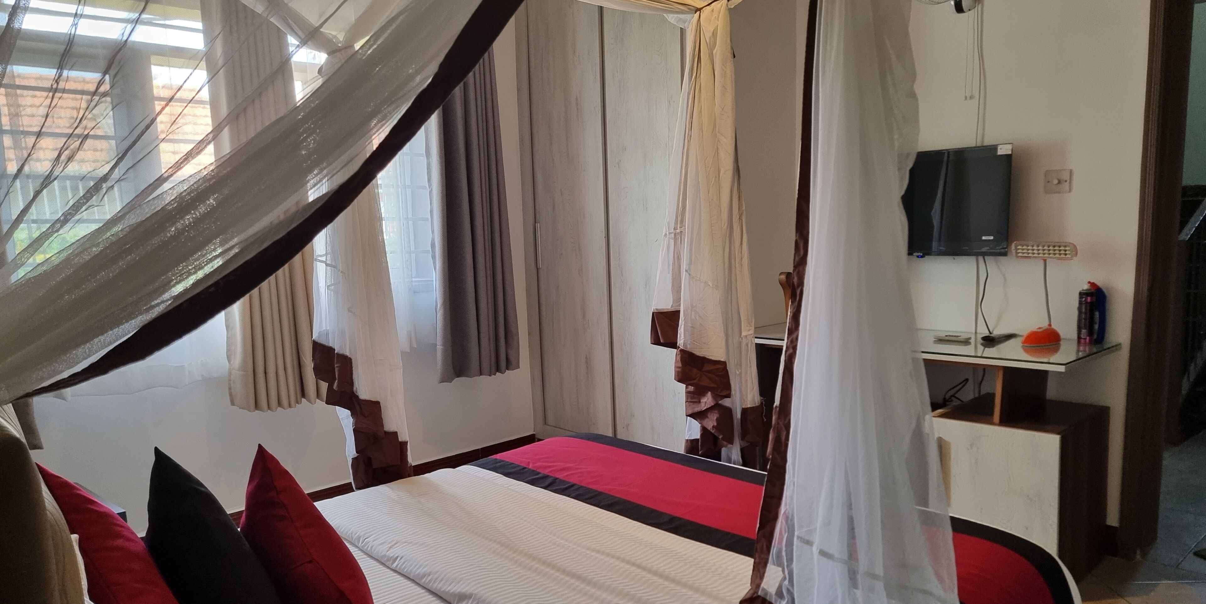 A bedroom with a bed, curtains, a television, and a bedside table.