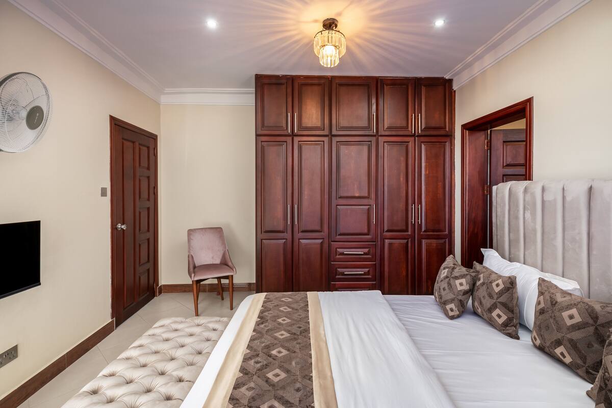 Quarto com cama, guarda-roupa, cadeira e televisão.