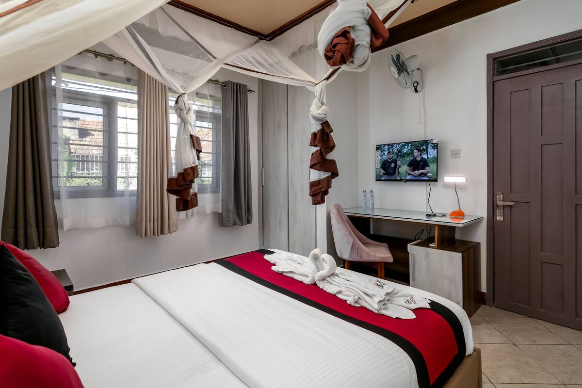 Quarto de hotel com cama, escrivaninha, cadeira, televisão e porta.