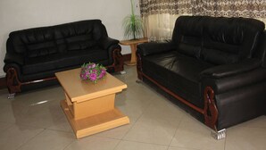 A living room with two black leather sofas, a wooden coffee table, and a small wooden side table with a plant. - Olorropil Hotel (Narok)