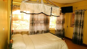A room with a bed, curtains, a television, and a window. - Olorropil Hotel (Narok)