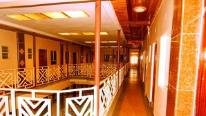 A corridor with a central walkway, wooden columns, patterned railings, and a tiled wall on one side. - Olorropil Hotel (Narok)