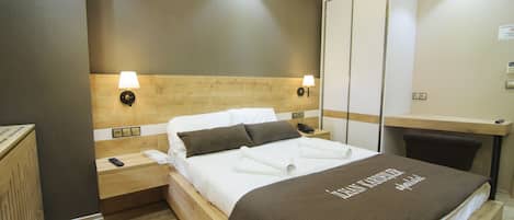 A modern hotel room with a wooden headboard, two bedside lamps, a neatly made bed with a brown blanket, and a wooden nightstand with a remote control.
