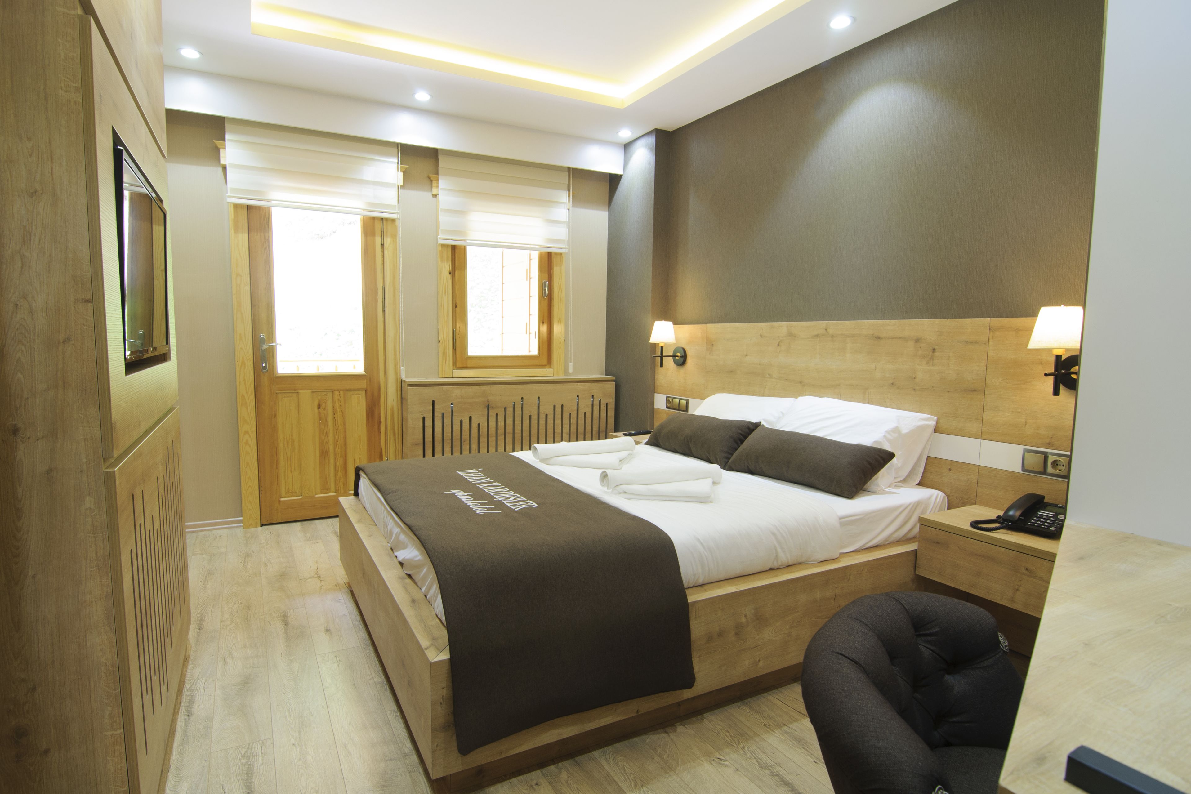 A hotel room with a wooden bed, a bedside table with a lamp, a telephone, and a window with blinds.