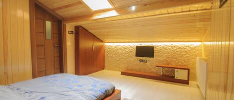 A bedroom with a bed, wooden walls, a skylight, a television, and a small bench.