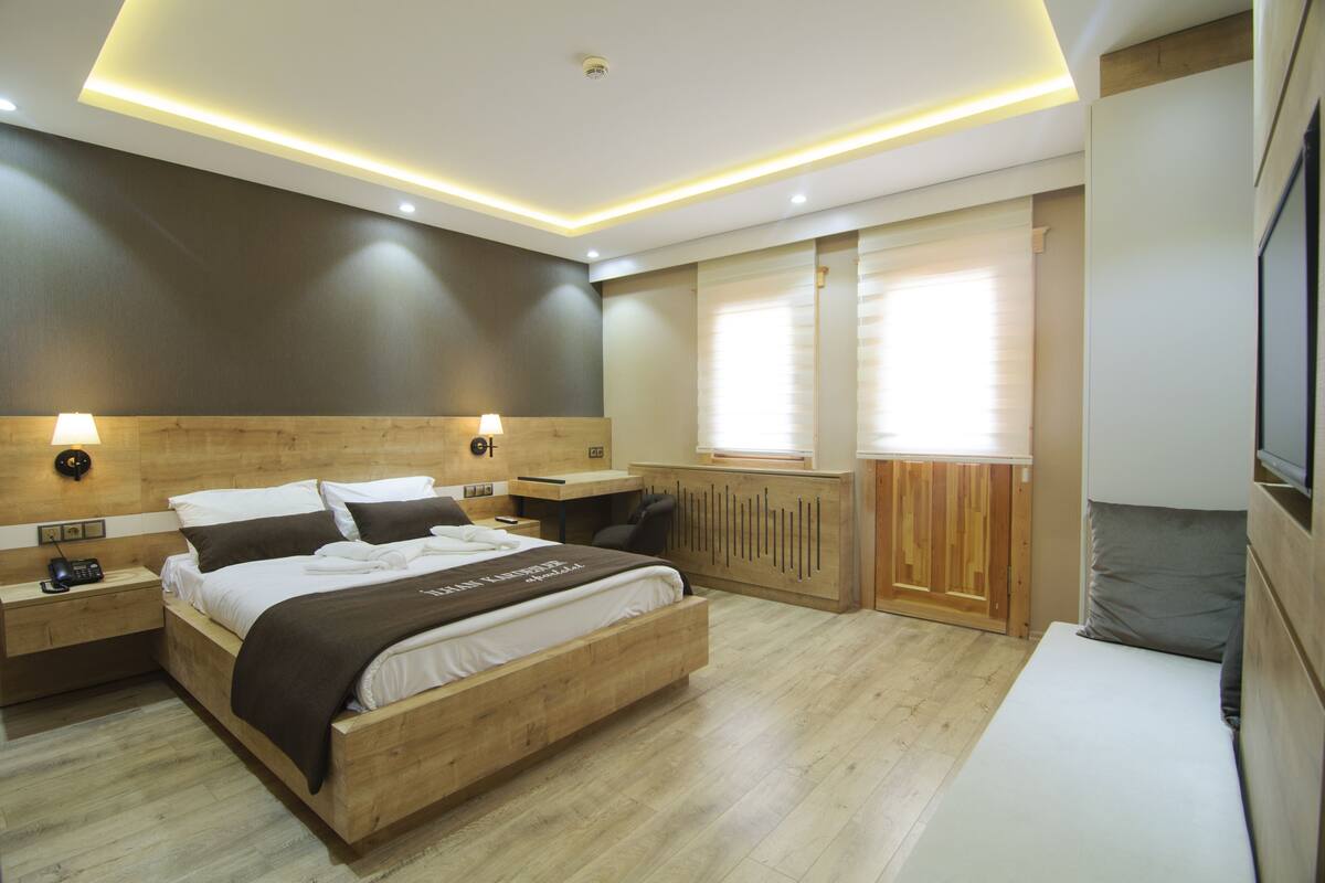 Ein modernes Schlafzimmer mit einem hölzernen Bett, Nachttischen, einem Schreibtisch und einem Fernseher.