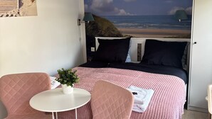 A bedroom with a bed, two pink chairs, a small table, and a potted plant. - B&B de Zandtaart (Egmond aan Zee)
