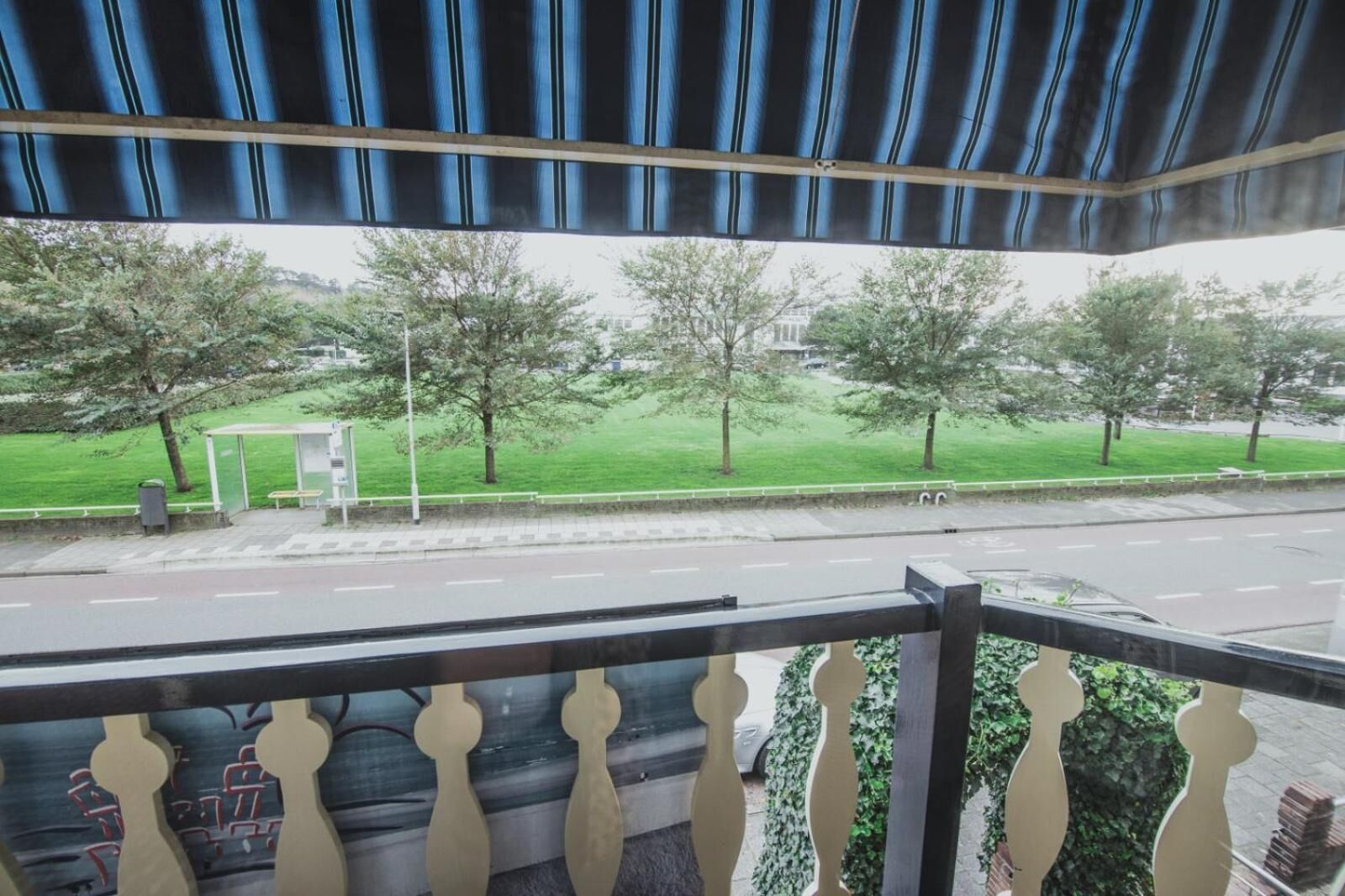 A balcony with a view of a green park, a bus stop, and a road.