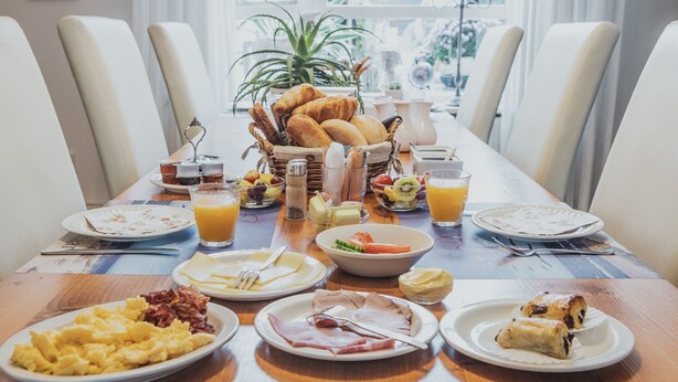 A breakfast setting with a variety of dishes including eggs, ham, pastries, and fruit. - B&B de Zandtaart (Egmond aan Zee)