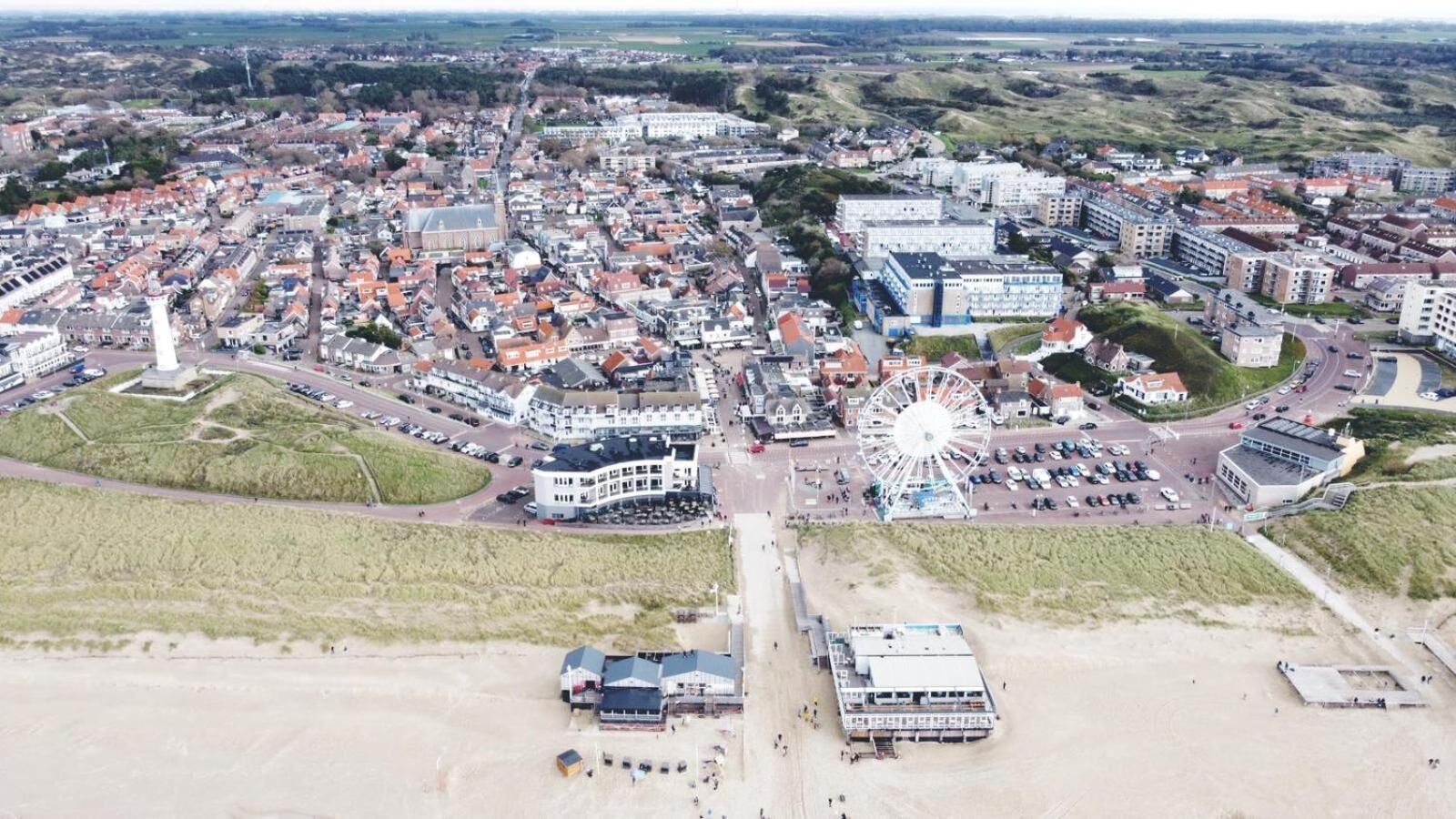 An aerial view of a coastal town with a prominent Ferris wheel, a historic church, and a sandy beach area.