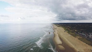 An aerial view of a beach with a long stretch of sand, a few people, and a distant town. - B&B de Zandtaart (Egmond aan Zee)