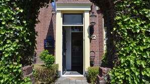 A brick building with a number 42 sign, a door, and a small garden area with bushes. - B&B de Zandtaart (Egmond aan Zee)