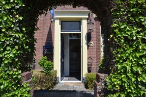 Un bâtiment en briques portant le numéro 42, avec une porte et un petit jardin agrémenté d’arbustes.
