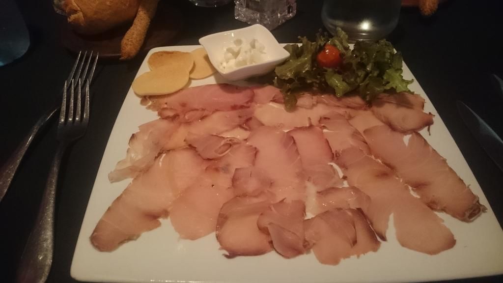 A plate with sliced ham, cheese, and a small bowl of sauce, accompanied by a side salad.