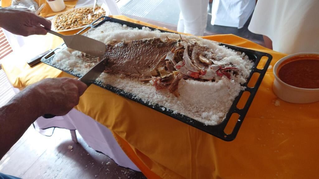 A person serving a large fish on a tray with rice and sauce.