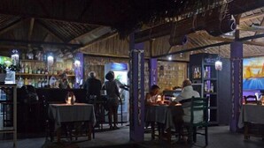 Un restaurant interior amb taules i cadires, una zona de bar i una pantalla gran que mostra una escena de ponent.
