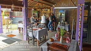 Un restaurant amb terrassa, taules i cadires, i una zona de bar amb barra i estantes plenes de botelles.