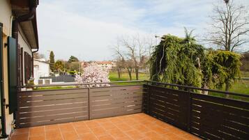 A balcony with a tiled floor, a metal railing, and a view of a park with trees and a building in the background.