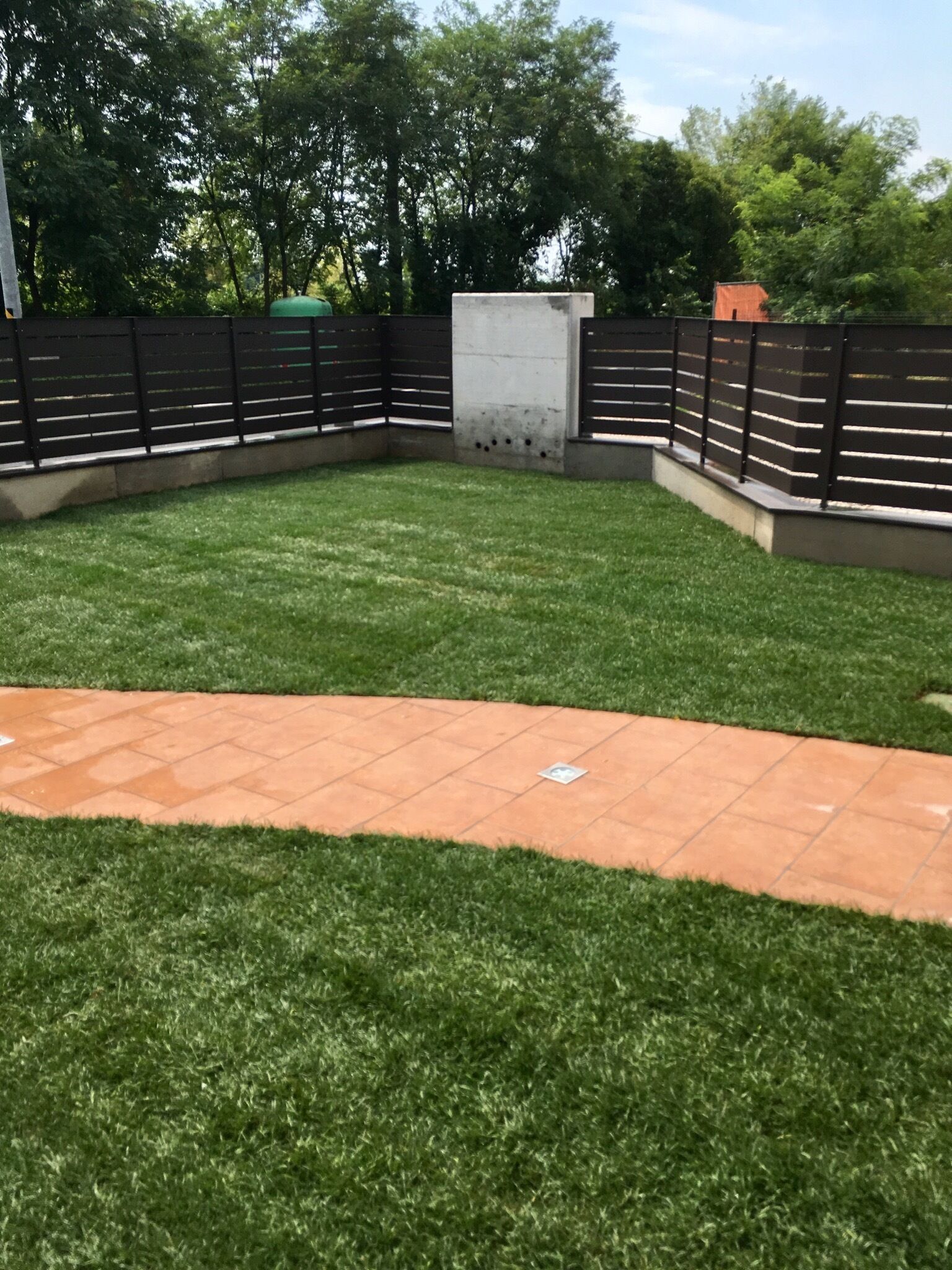 A fenced backyard with a paved patio area and a grassy lawn.