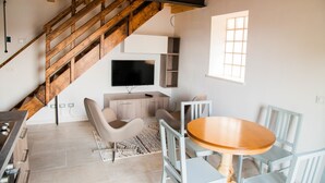 A modern living room with a wooden staircase, a flat-screen TV, a dining table with chairs, and a patterned rug. - Gate To Verona (Verona)