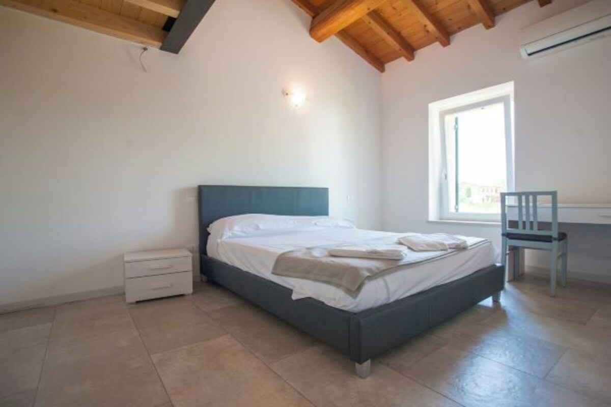 A bedroom with a bed, a chair, a desk, and a window.