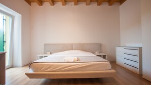 A modern bedroom with a large bed, bedside tables, a dresser, and a window. - Gate To Verona (Verona)