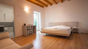A bedroom with a large bed, wooden flooring, a desk, and a chair.