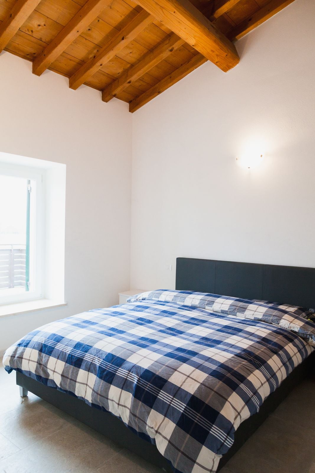 Un dormitorio con cama, ventana y techo de madera.