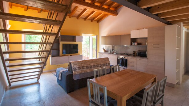 A modern kitchen with wooden beams, a dining area with a table and chairs, and a staircase leading to an upper level. - Gate To Verona (Verona)