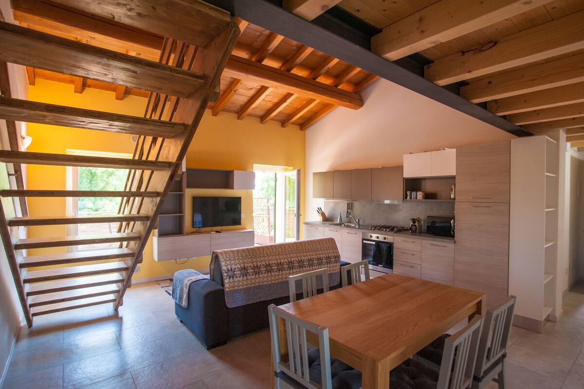 Eine moderne Küche mit Holzbalken, ein Essbereich mit Tisch und Stühlen sowie eine Treppe zu einer oberen Ebene.