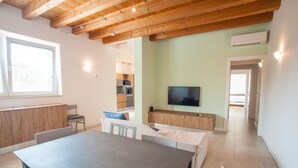 A modern living room with a dining table, chairs, a TV, and a kitchen in the background. - Gate To Verona (Verona)
